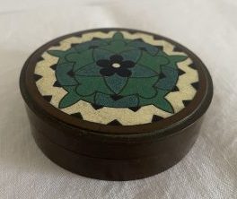 Photograph of a round dark metal box with enamelled inlaid lid in green and white